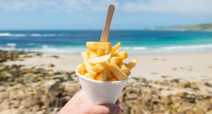 person holding French fries on the beach