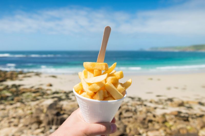 person holding French fries on the beach