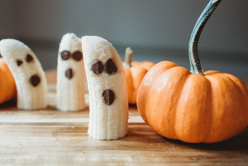 Bananas cut in half with chocolate chips for eyes and mouth, to look like a ghost, with small pumpkins on the side.