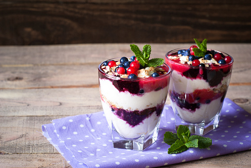 Healthy layered dessert with yougurt, granola, jam, red currant and blueberries on wooden background with space for text