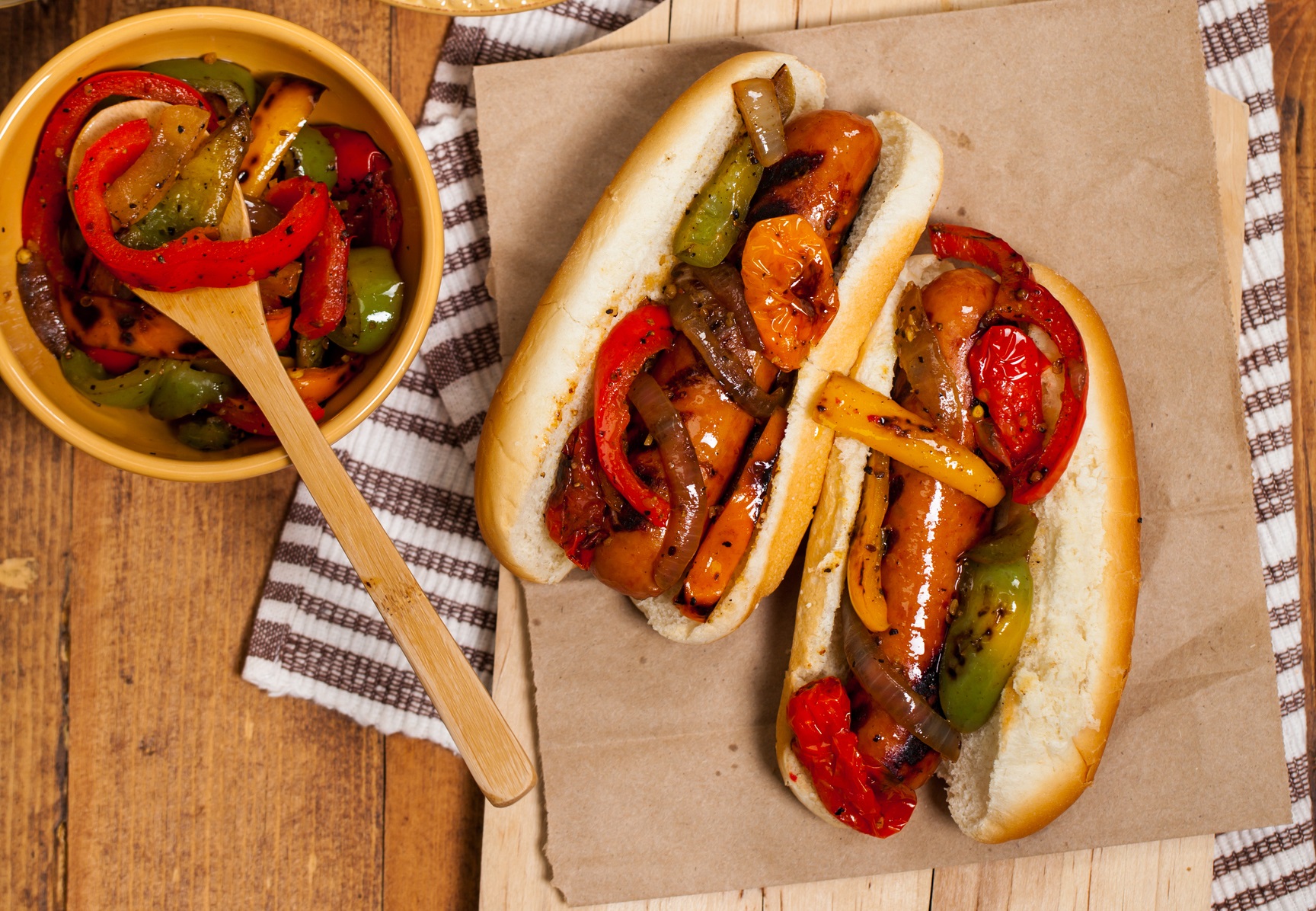 Two chicken sausage sandwiches with roasted peppers, and peppers in a bowl.