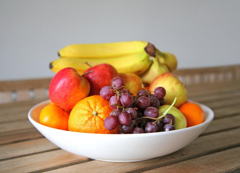 a bowl of fresh fruit set on a wooden table