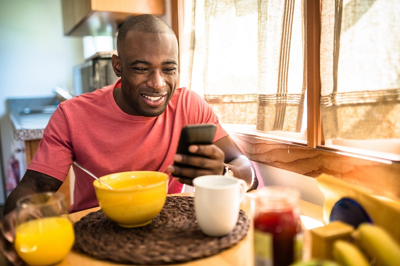 man on his smart phone while eating breakfast during the week