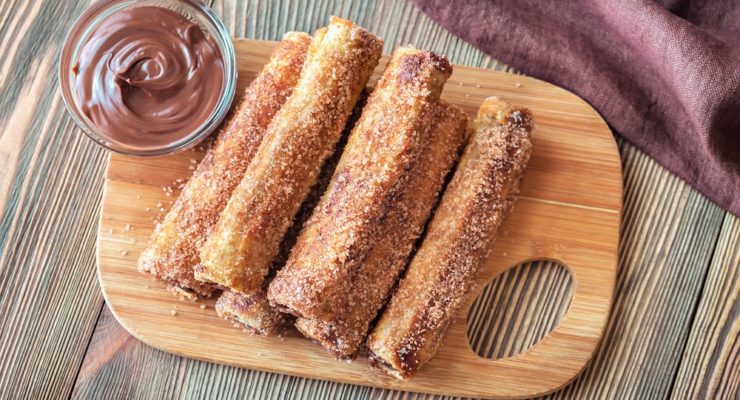 French toast roll-ups on a wooden board with chocolate sauce