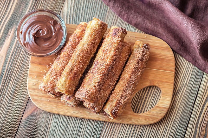 French toast roll-ups on a wooden board with chocolate sauce
