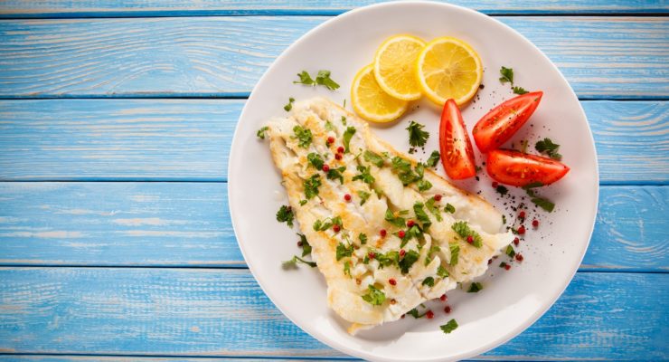 white fish on a plate with lemons and tomatoes