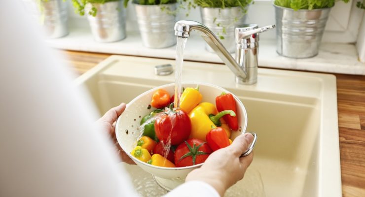 woman washing peppers in a colander in the sink