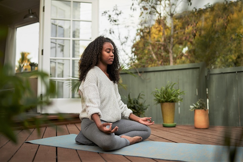 A woman meditating outdoors on a yoga mat to help stress