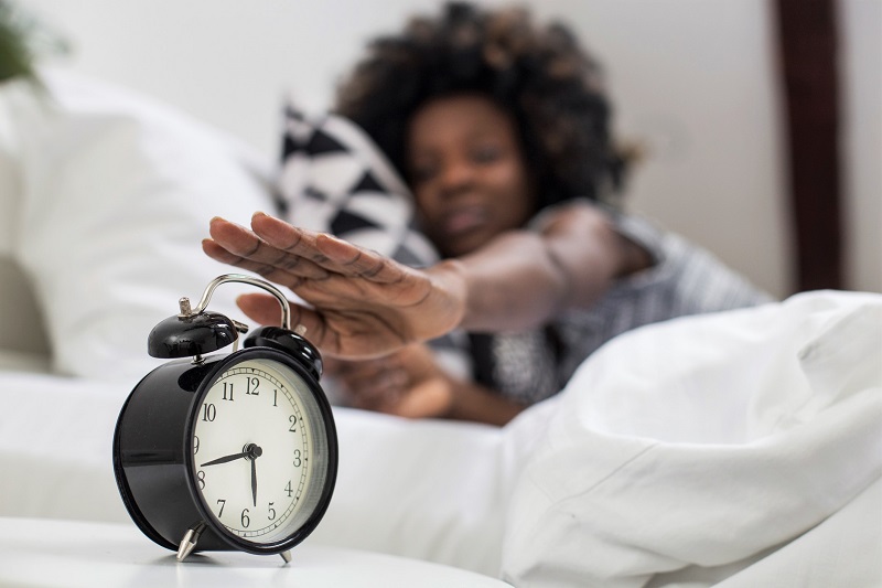 A woman pressing the snooze button early in the day to get better sleep.