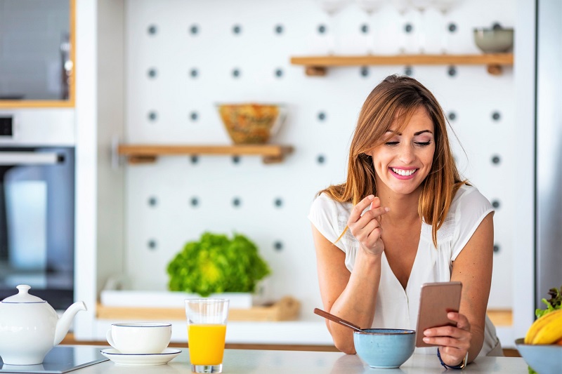 a woman eating breakfast and looking at her phone on a personalized program.