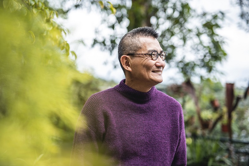 an older man in a warm purple sweater smiling outdoors