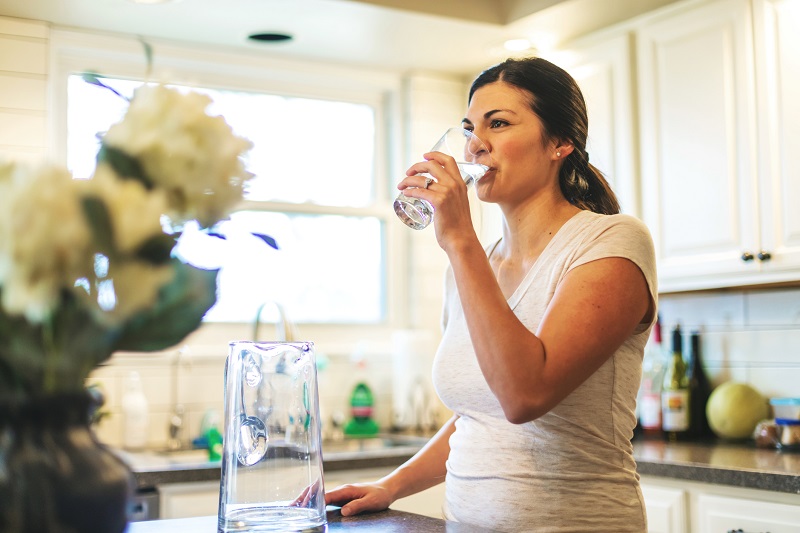 woman drinking glass of water in kitchen. metabolism boosting tips for women