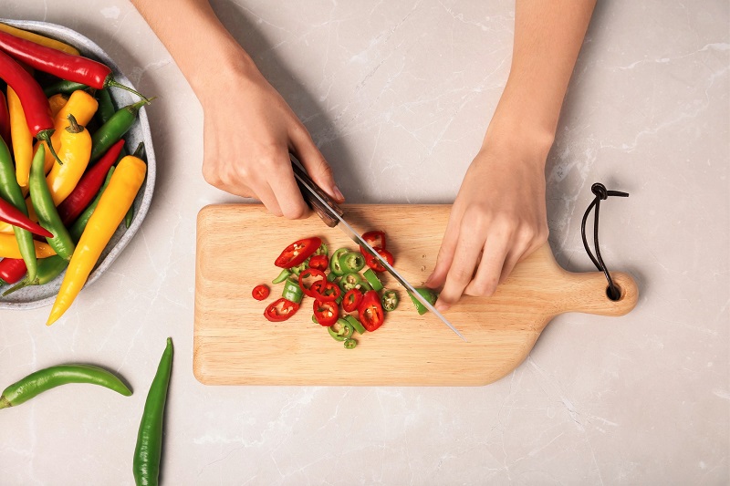Woman cutting chili peppers at table, top view. metabolism boosting tips for women