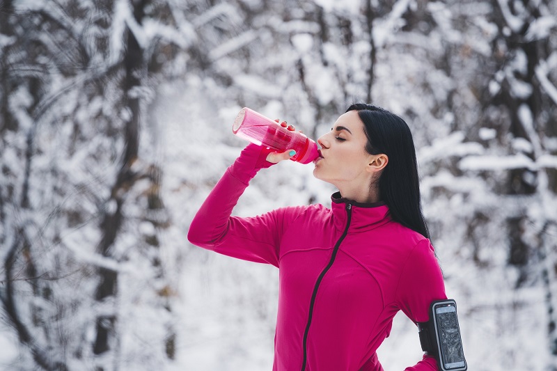 a woman taking a break from winter workouts by drinking some water