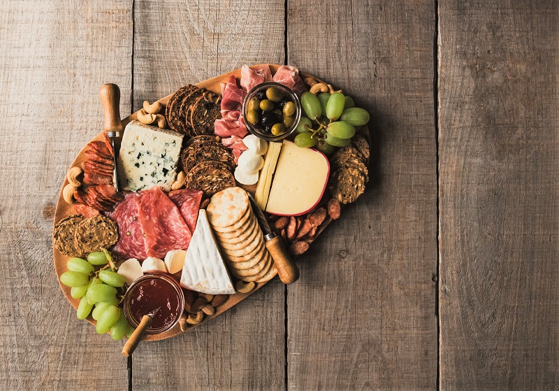 a spread of cheeses, crackers meats, and grapes on a charcuterie board