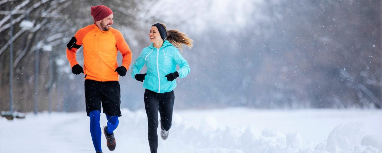 a woman and a man running doing winter workouts, surrounded by snow