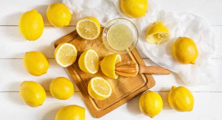 fresh lemons and a bowl of unlimited lemon juice on a cutting board with a handheld juicer