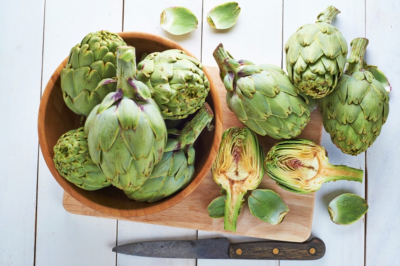 fresh artichokes on a cutting board and in a bowl