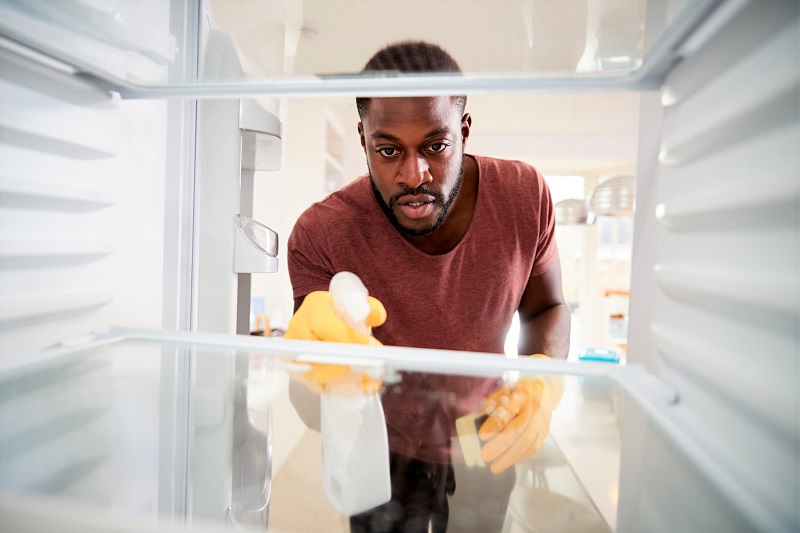 man spring cleaning the inside of his kitchen refrigerator