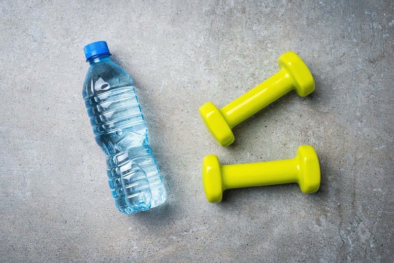 a water bottle and two dumbbells against a gray background