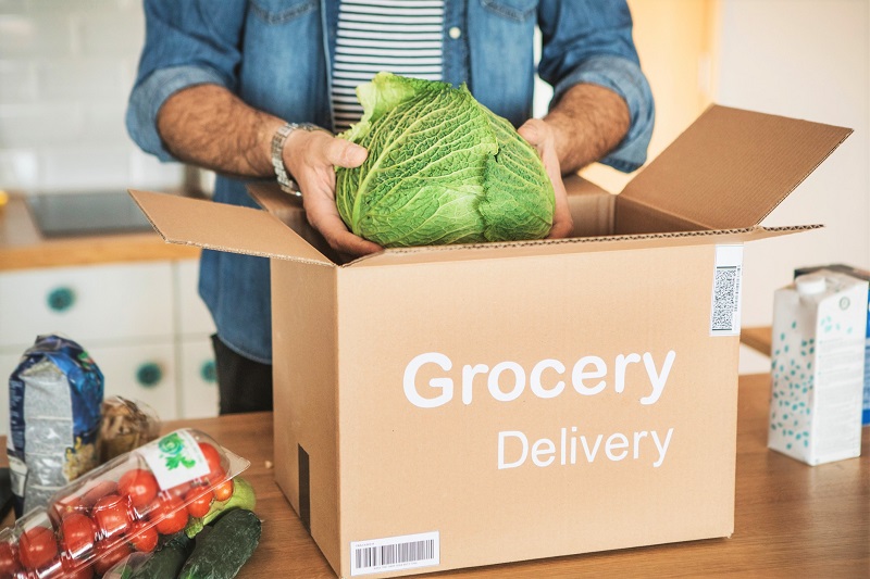 : Man unpacking a cabbage from an online grocery delivery box