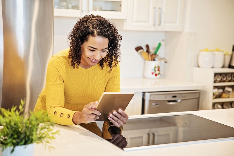 Woman leaning on kitchen counter while looking at a tablet 