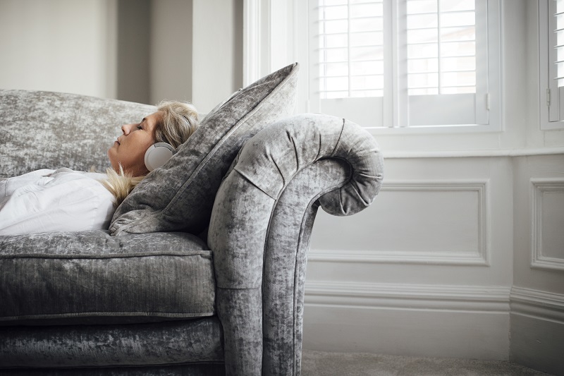 a woman resting on a gray couch with her headphones on for stress relief