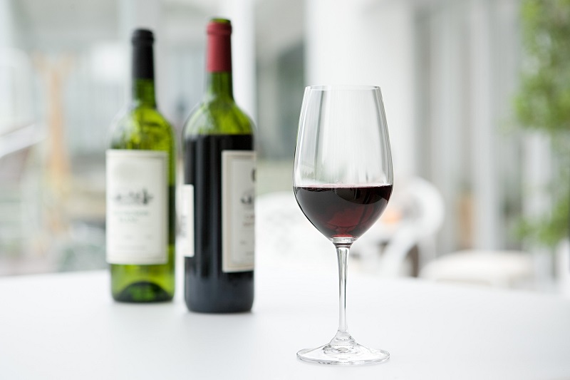 two bottles of wine and a glass with half-filled red wine on a table
