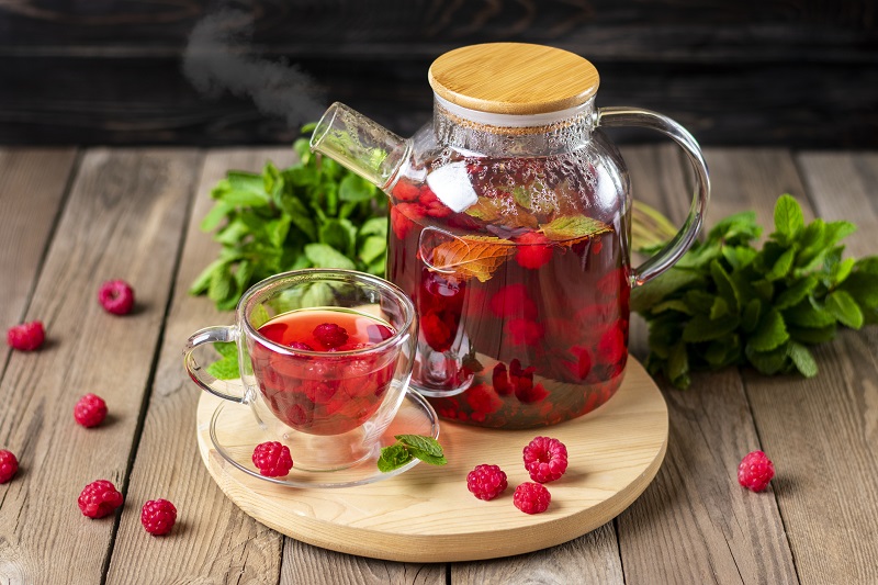 Herbal tea with berries, raspberries, mint leaves and hibiscus flowers in glass teapot and cup on wooden table 