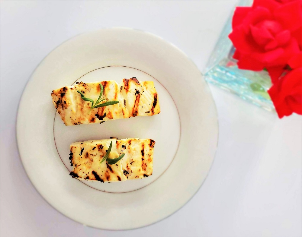 two Grilled Rosemary Halibut fillets on a plate next to red flowers