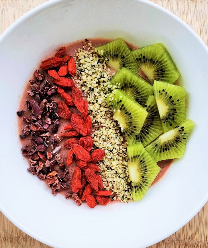 Strawberry Superfood Smoothie Bowl topped with kiwi, hemp seeds, cacao nibs, and goji berries