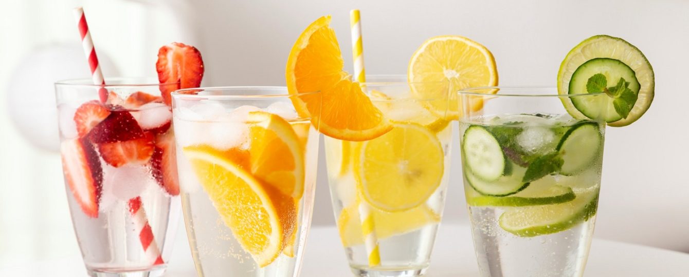 Strawberry infused water, orange infused water, lemon infused water, and cucumber infused water on a white table.