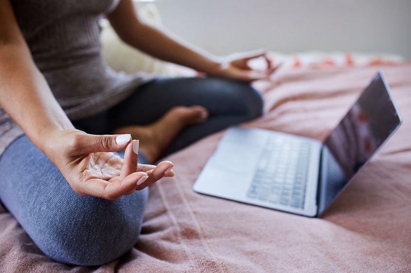 Woman is sitting on her bed streaming an online meditation class