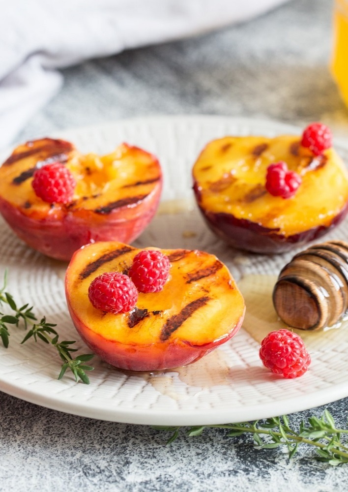 Ripe grilled peaches with honey and raspberries on a plate