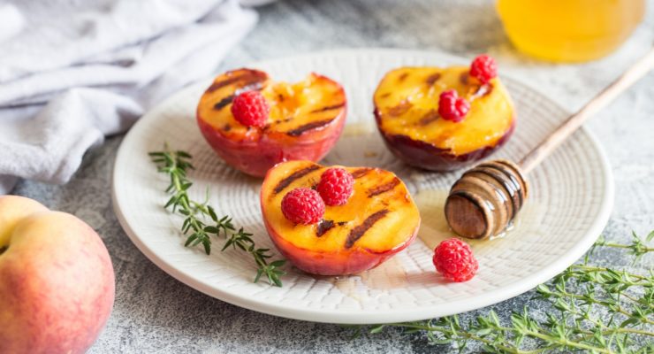 Ripe grilled peaches with honey and raspberries on a plate