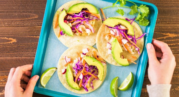 Fresh fish tacos on a tray with avocado, cabbage and limes