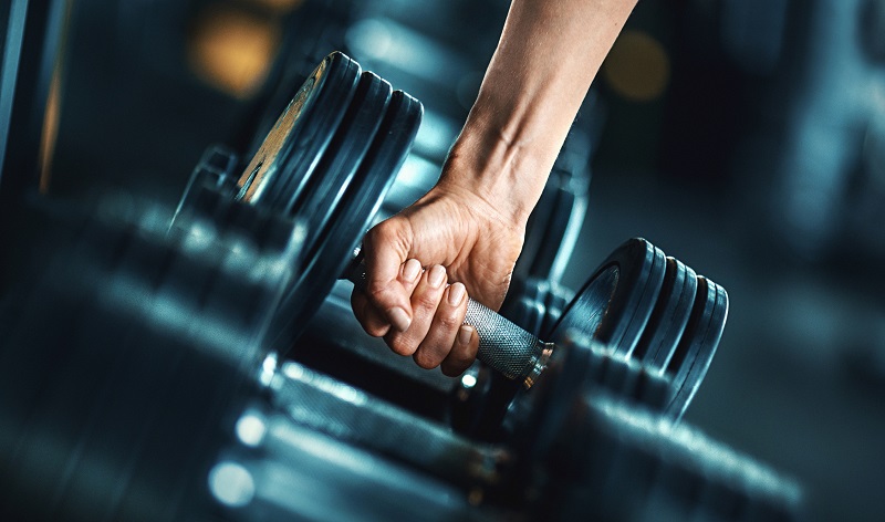 Closeup side view of unrecognizable woman grabbing a dumbbell for activities