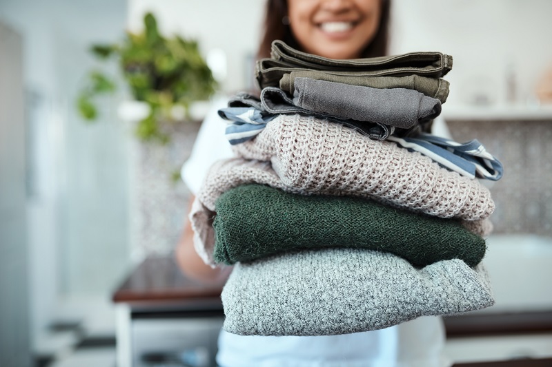 woman doing laundry activities and holding a pile of folded laundry at home