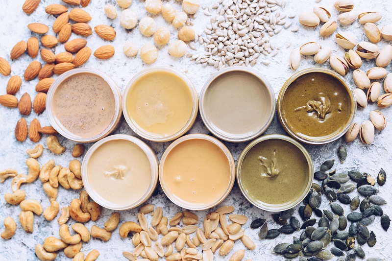 Nuts and seeds and their butter in jars with ingredients. Homemade raw organic peanut, almond, hazelnut, cashew, pistachio, macadamia nuts paste and sunflower and pumpkin seeds butter on a table.