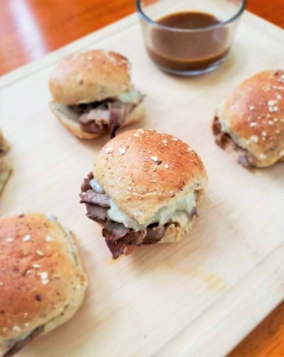 Five French dip sliders next to au jus