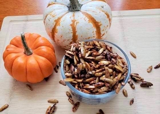 Sweet and Spicy seasoned Roasted Pumpkin Seeds in a bowl next to small pumpkins