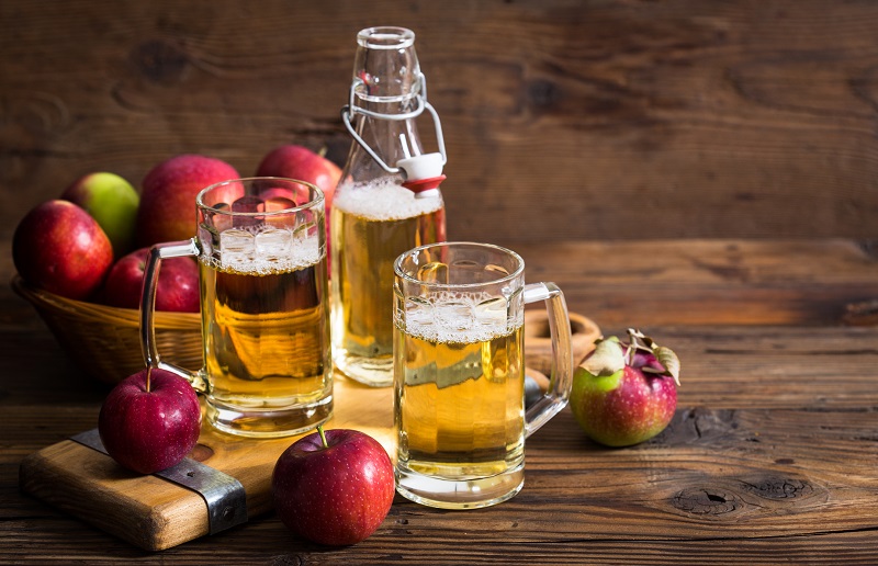 Three glasses of apple cider surrounded by fresh apples