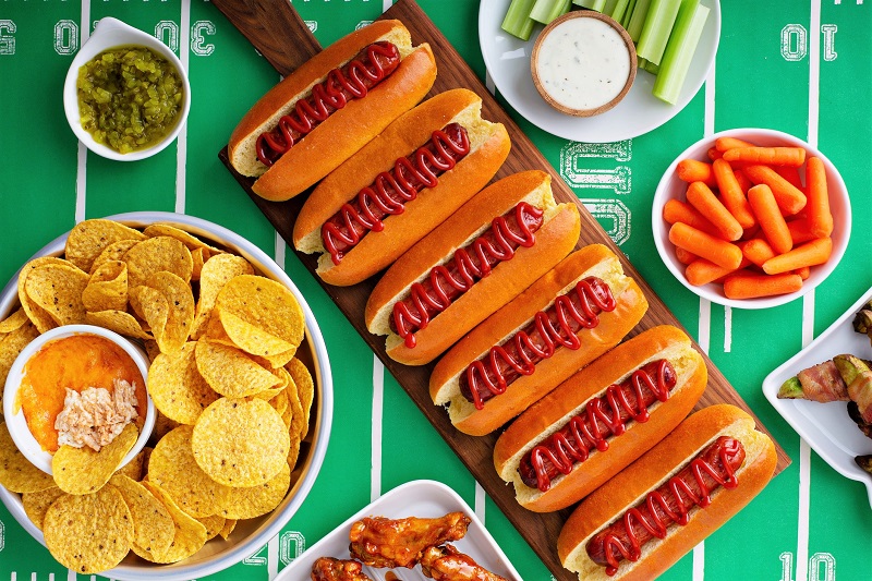 A full spread of chips and dip, veggies and dip, and hot dogs