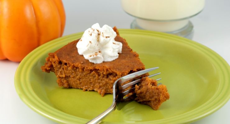 Fork cutting into a fresh slice of pumpkin pie topped with whipped cream