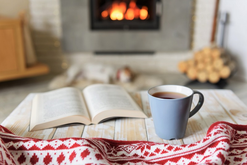 reading a book and drinking tea by the fireplace in winter