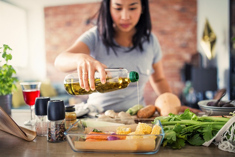 woman pouring cooking oil over vegetables