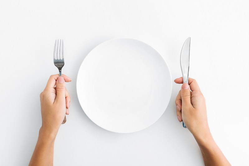 Hands holding a knife and a fork with an empty plate
