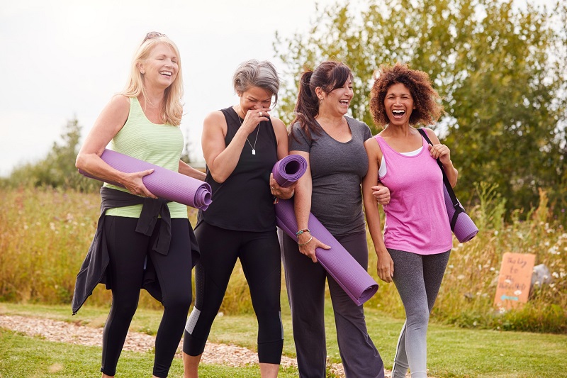 Group of four women walking and laughing with yoga mats