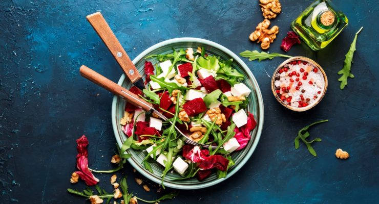 A bowl of healthy arugula salad with fruit, walnuts, and toppings