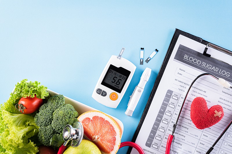 A glucose reader next to a bowl of vegetables and a stethoscope